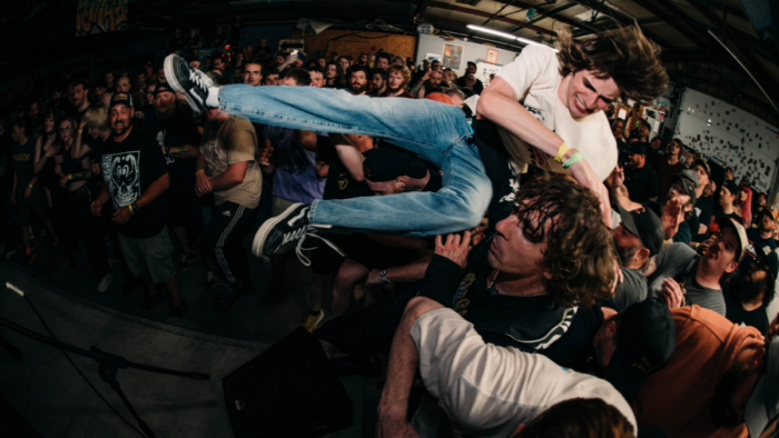 A man is held up by audience members in a mosh pin at a concert.