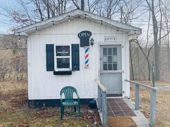 A little building that looks like a shed sits with Christmas lights around it and a hair shop pole decal on the front of it. 