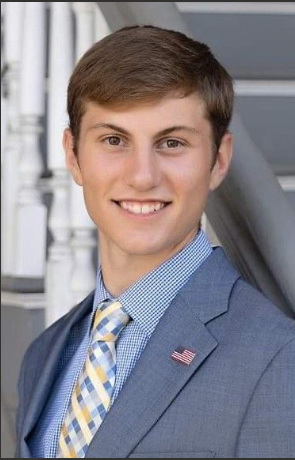 A young man smiles for a photo while wearing a formal suit. 