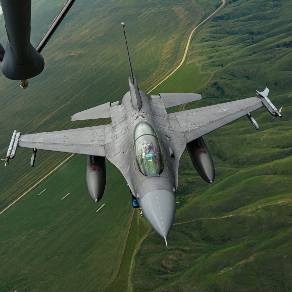 A fighter jet flying above green fields and rugged terrain