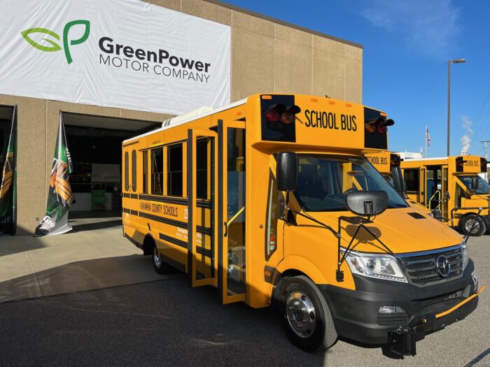 A small yellow school bus sits in front of an open garage bay with a white banner hanging over it.