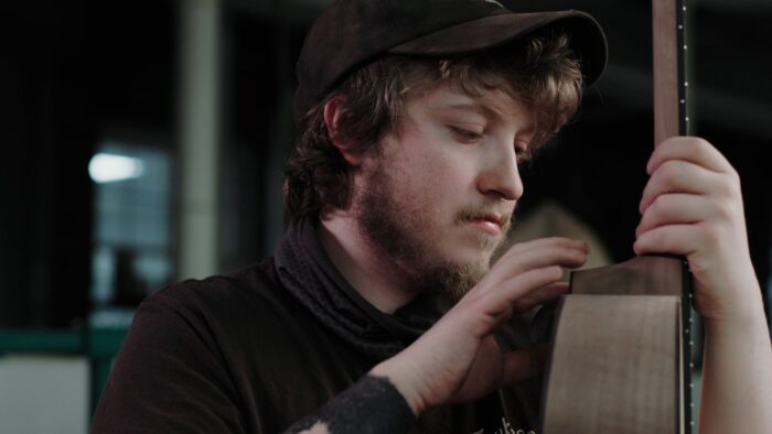 A close up of a young man working on a guitar.