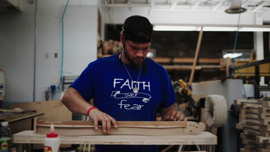 A an adult man wearing a blue shirt that reads, "Faith over Fear," works on a dulcimer.