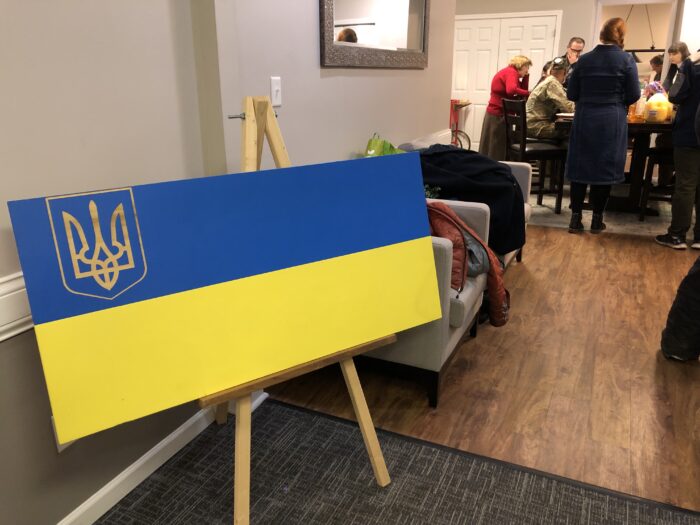 A Ukranian flag, with blue on top and yellow on bottom, as well as a traditional tryzub or trident in the top left corner. In the background can be seen some of the people that attended the gathering.