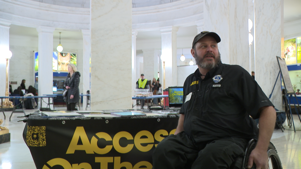 A man in a wheel chair sits in front of a table that says access on the go.