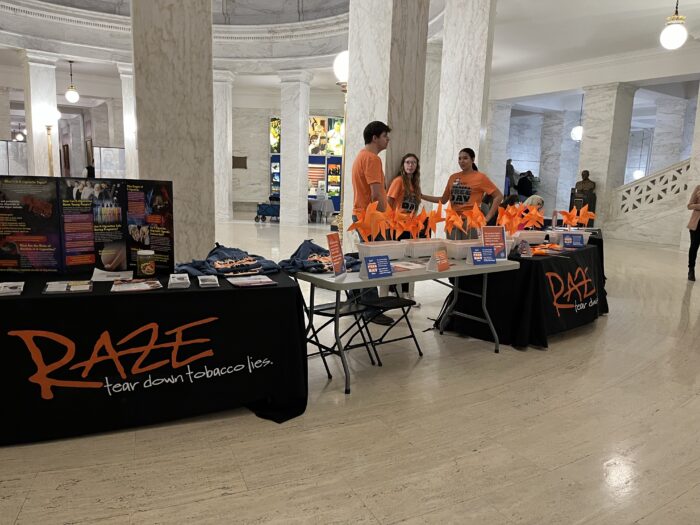 A group of students mans a table of information about being tobacco free. They are wearing orange t-shirts.