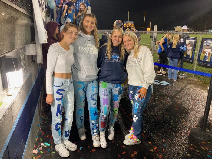 Four teen women show off their "senior jeans" at a football game. 