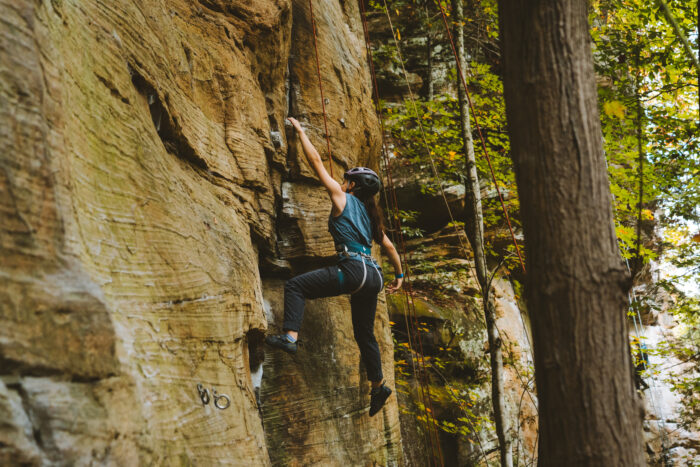 A woman in a blue shirt climbs a rock face.