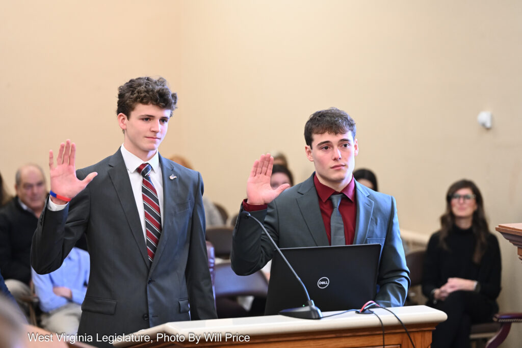 Two teenage boys with brown hair raise their right hands to swear in before giving testimony at a committee meeting.