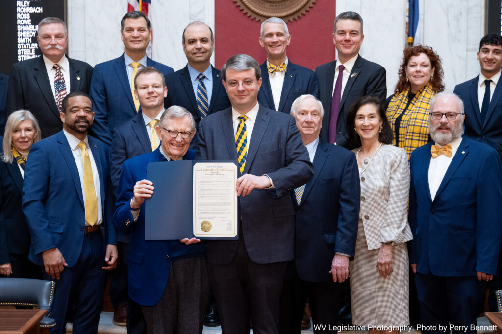Smiling men and women dressed in blue and gold holding a proclamation.