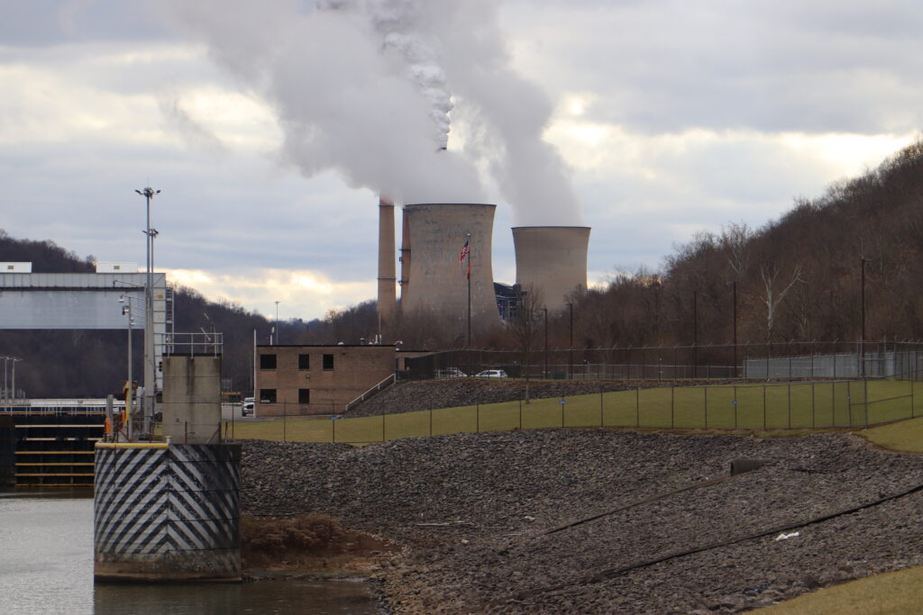 Steam rises from the concrete cooling towers of a coal-burning power plant against a gray sky.