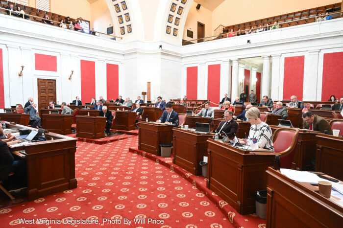 A picture of a legislature with wooden desks and people sitting at them.