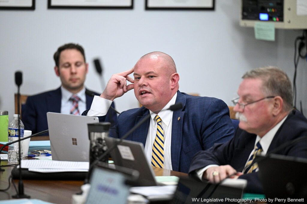 Delegate Brandon Steele sits behind a desk at the House Judiciary Committee. He has his laptop open, and other delegates sit on either side of him. He is holding his hand to his face, and sitting with his mouth slightly open.