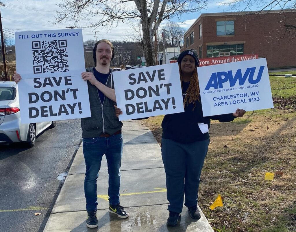 Postal workers hold signs that read "Save Don't Delay."