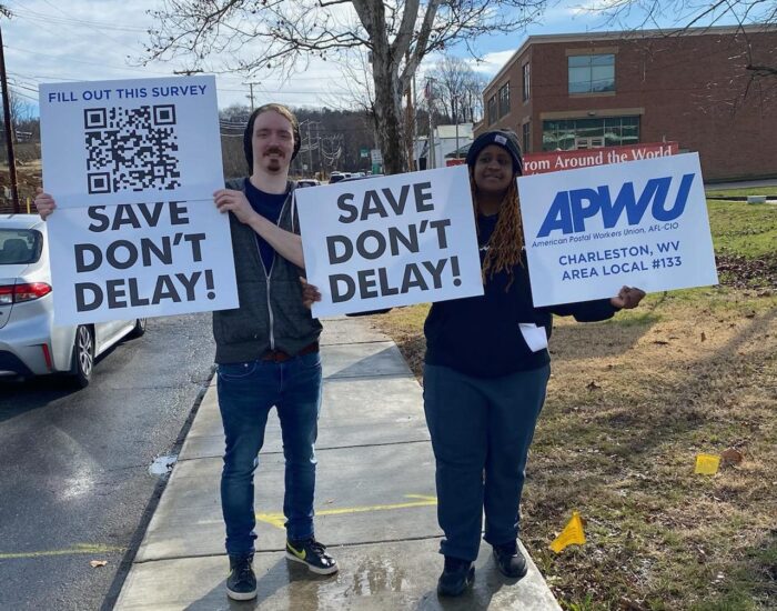Postal workers hold signs that read "Save Don't Delay."