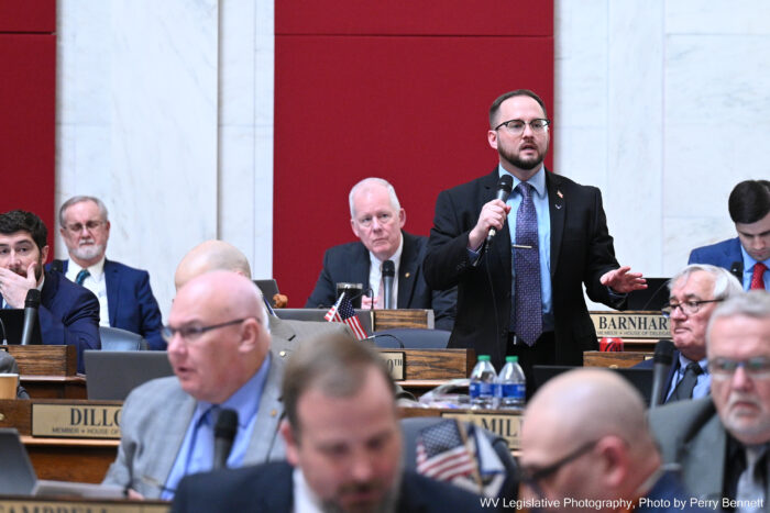 Man with beard and glasses speaks among several other sitting people
