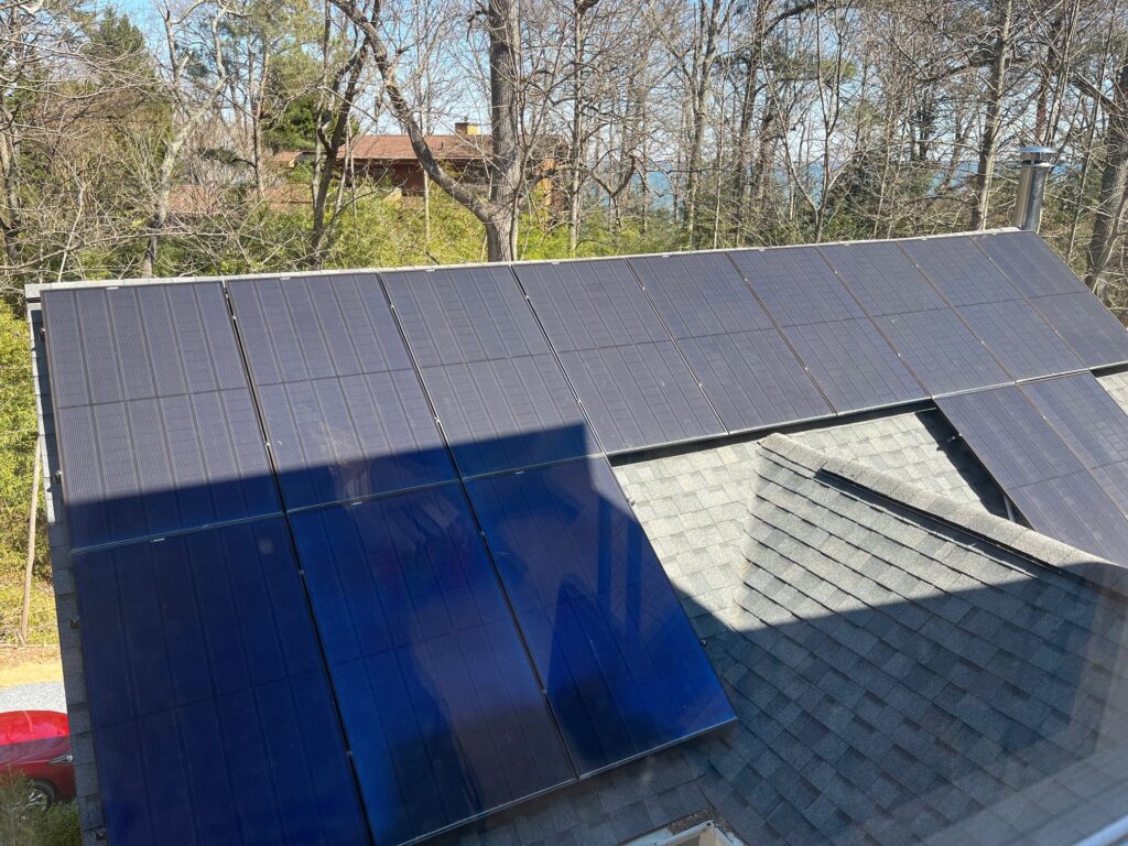Solar panels mounted to a rooftop generate electricity on a sunny day in a wooded area.