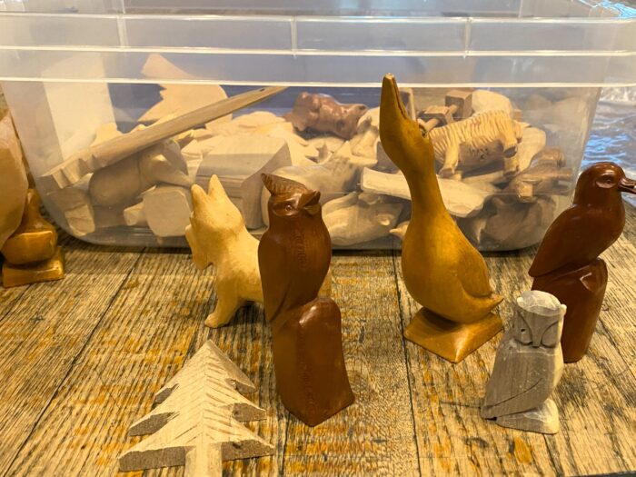 Finished and in-progress carvings sit in front of a box of wood “blanks” or “patterns.”