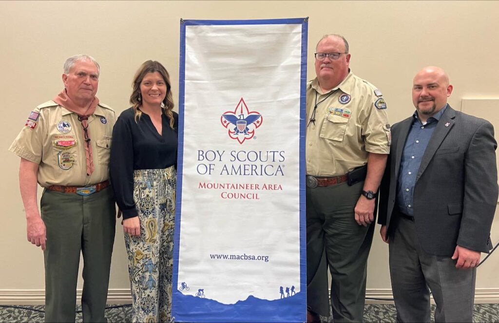 Amy Garbrick stands beside three fellow scouting leaders and a sign that says "Boy Scouts of America Mountaineer Area Council."