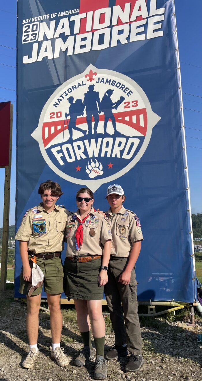 Amy Garbrick and her sons Tyler and Ethan stand before a sign that says "Boy Scouts of America National Jamboree." They are wearing scouting uniforms.