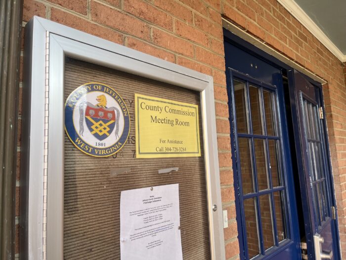 Signs posted to a bulletin board outside of the Jefferson County Courthouse display the county seal, a sign, a sign on meeting times and a sign on the location of the meeting room within the building.