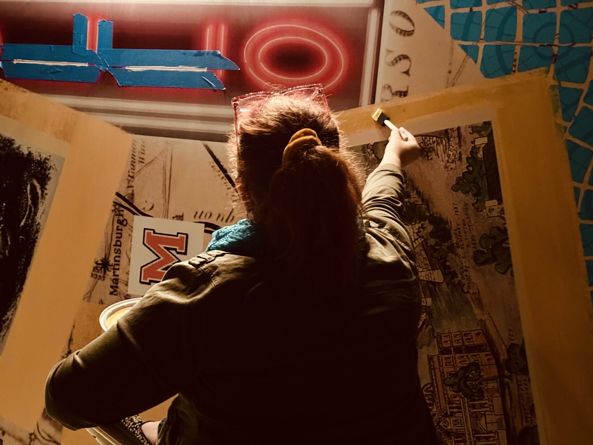 A woman with a scarf paints a portion of a mural.