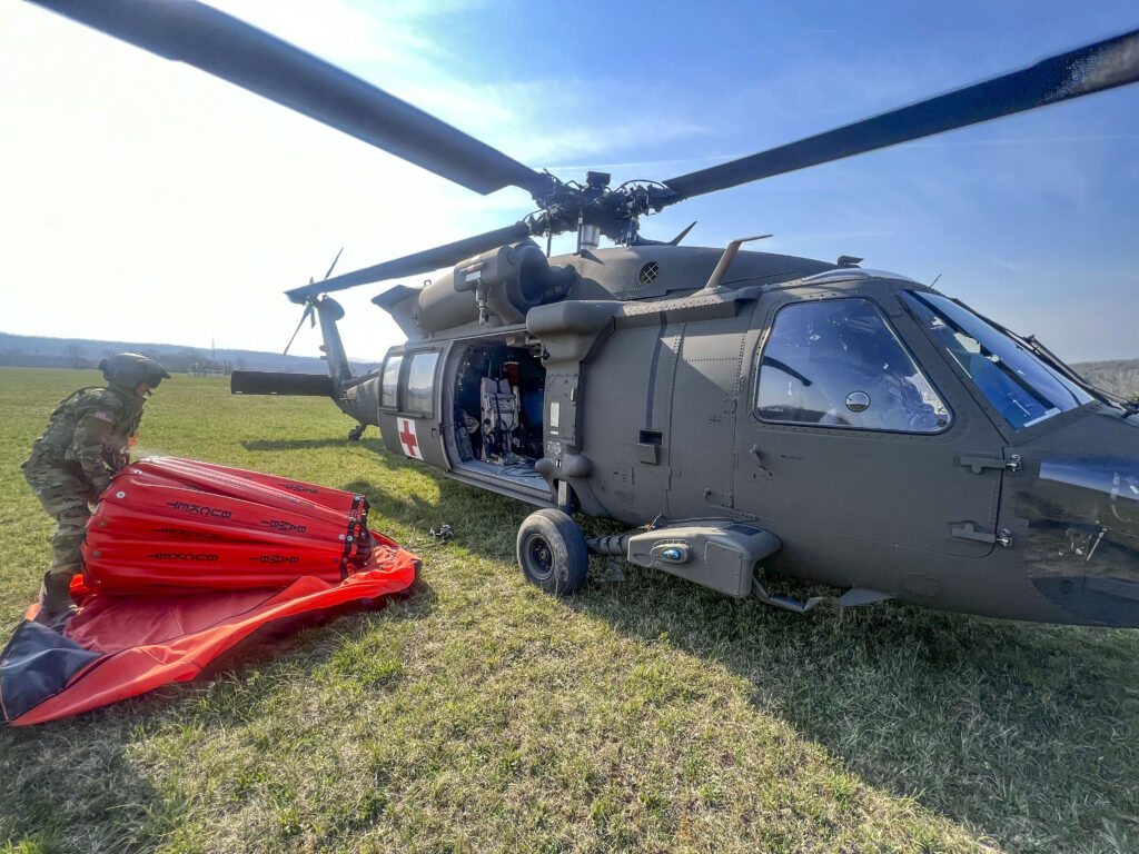 A uniformed National Guard personnel prepares equipment for a helicopter.
