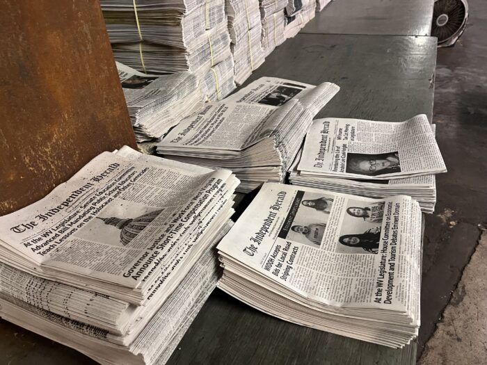 Stacks of newspapers are seen on a table. At the top of each stack reads, "The Independent Herald."