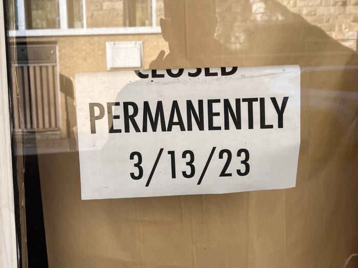 A sign on a glass window reads, "Closed Permanently, 03/13/2023."