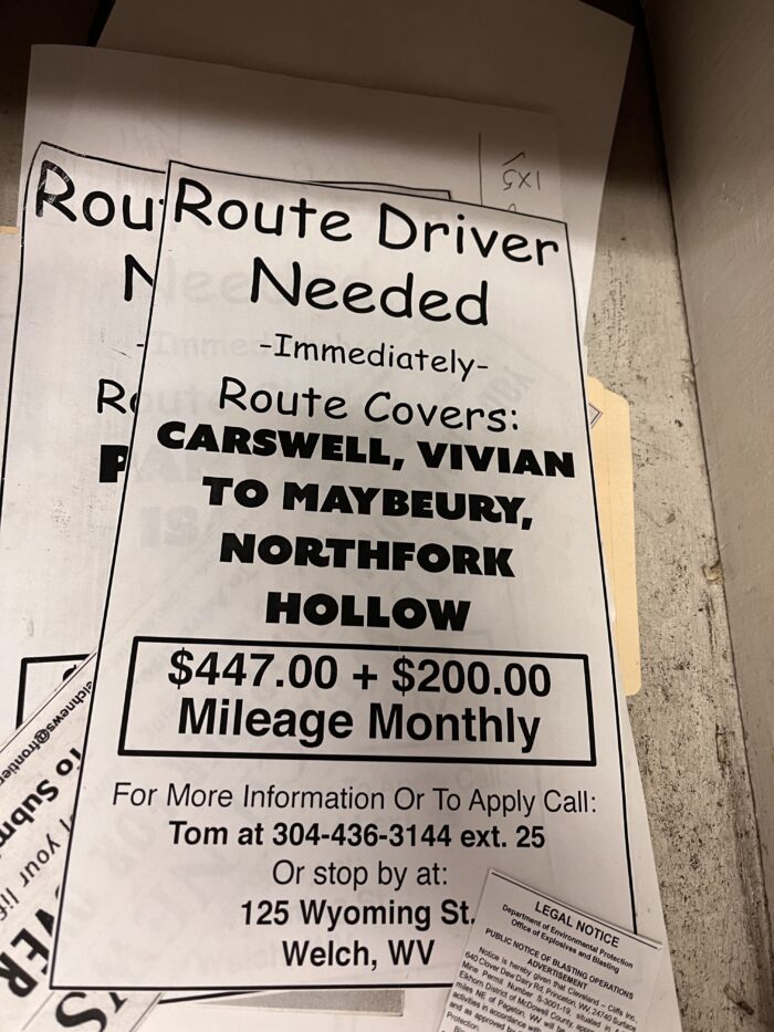 Papers are shown on a table. They read, "Route Driver Needed Immediately. Route Covers Carswell, Vivian to Maybeury, Northfork Hollow. $447.00 + $200.00 Mileage Monthly. For more information or to apply, call Tom at 304-436-3144, ext. 25. Or stop by at 125 Wyoming Street, Welch, WV."