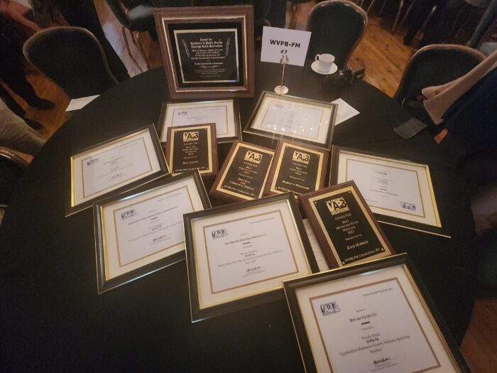 An overhead photo showing 12 awards on a table with a black tablecloth. The awards are either plaques or framed certificates.