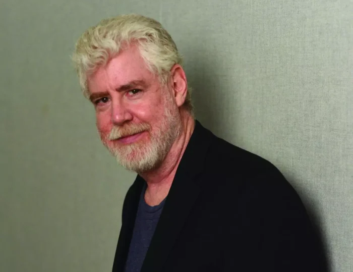 An older man with white hair poses for a headshot. He wears a black blazer and navy shirt.