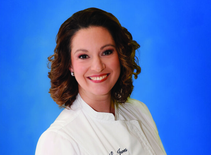 Woman in white chef's attire poses for a photo in front of a blue background.