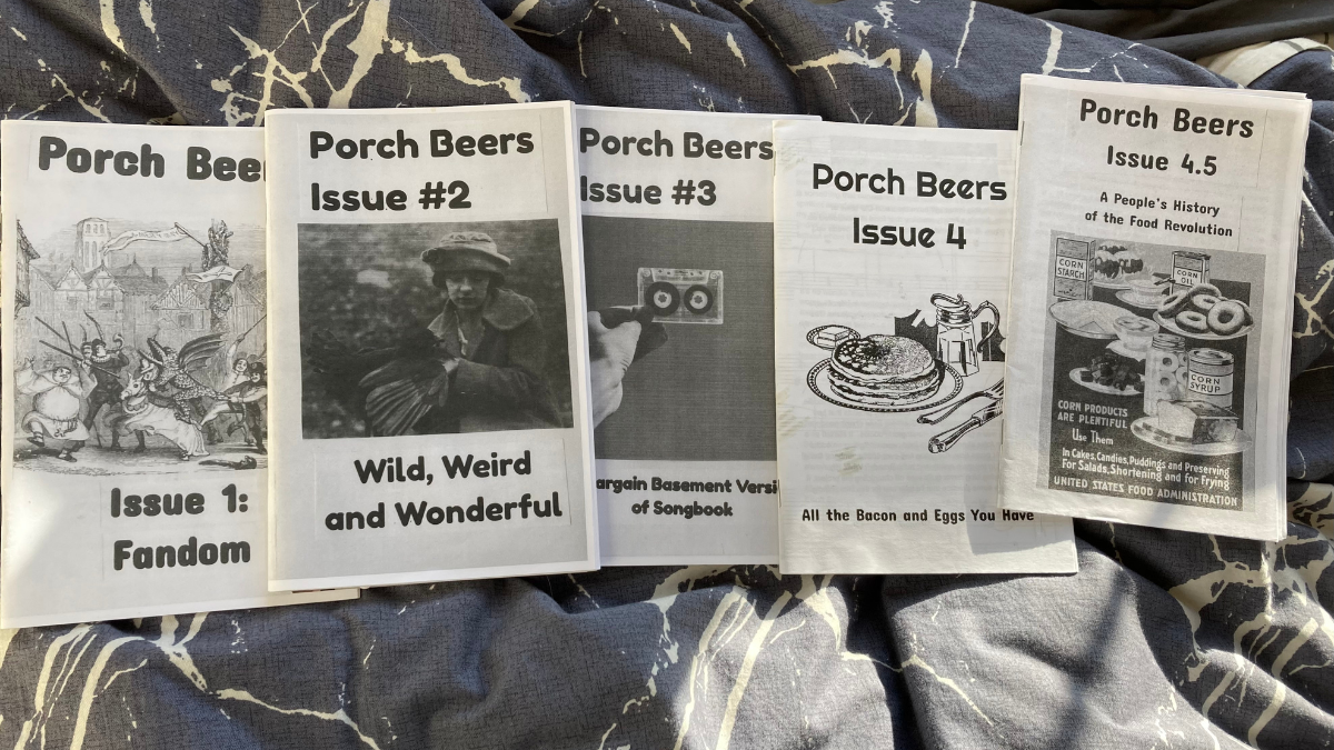 Five zines printed on paper and in black and white are shown side by side on a blanket. Each of the four issues reads, "Porch Beers" at the top, and then Issue #1, #2, #3, #4, and #4.5. One issue reads, "Fandom," another reads, "Wild, Weird and Wonderful," another reads, "Bargain Basement Version of a Songbook," another reads, "All the Bacon and Eggs You Have," and the fifth one reads, "A People's History of the Food Revolution."