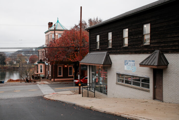 A building is seen along a street in the fall. In the distance is a pretty tree with red leaves. On the side of the building is a sign that reads, "The Seeing Hand."