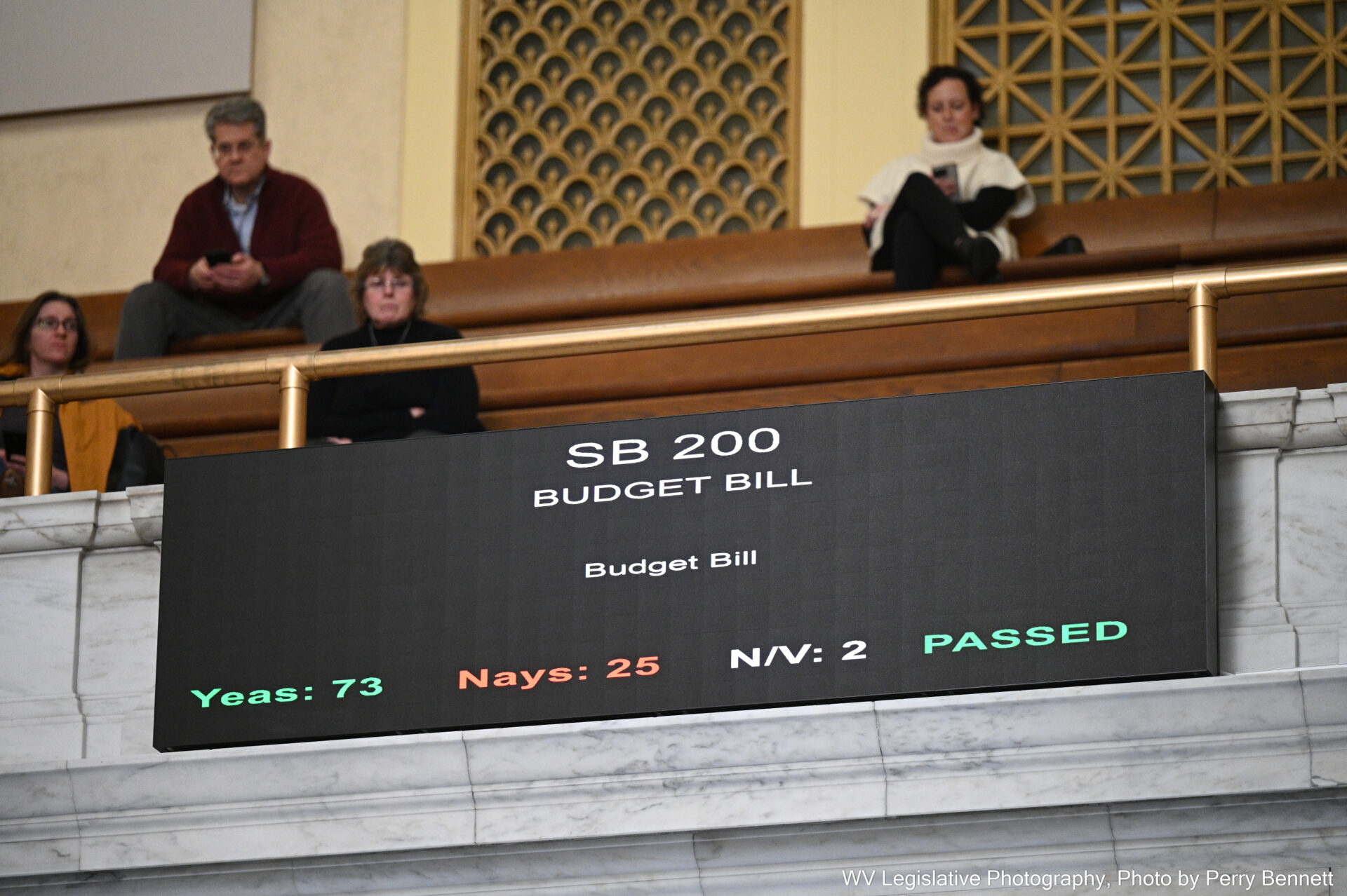 A screen displays a legislative budget bill and the votes cast by lawmakers. The votes read 76 yeas, 25 nays, and 2 absent or not voting. The screen also indicates the bill passed.