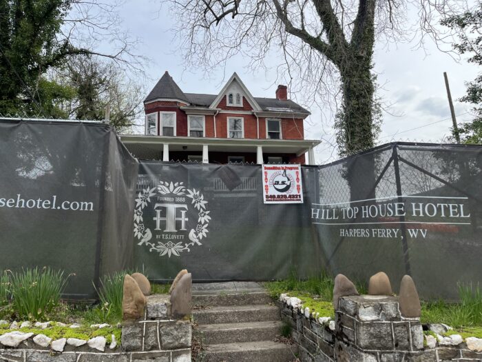 Stone stairs lead to a red townhouse, which is blocked off by a fence displaying advertisements for Hill Top House Hotel.