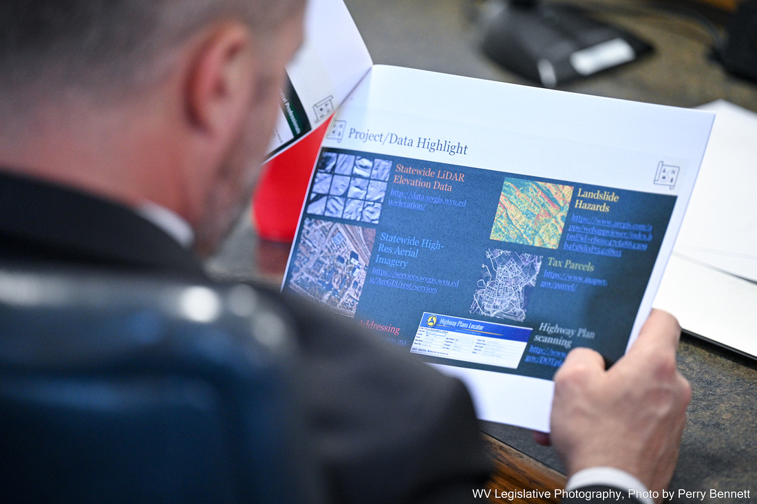 A man reviews a packet of papers with a powerpoint printed on it. The powerpoint slides show different technology for a new flood risk assessment database, including landslide risk and tax parcel data.