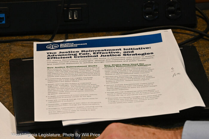 A packet of paper sits on a desk. Its title reads "The Justice Reinvestment Initiative; Advancing Fair, Effective, and Efficient Criminal Justice Strategies."