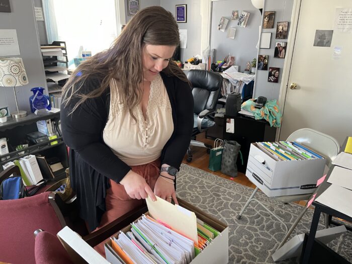 A woman sorts through a box of files labeled in colorful folders.