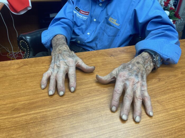 A man's elderly hands are shown on a desk. They look worn and worked.
