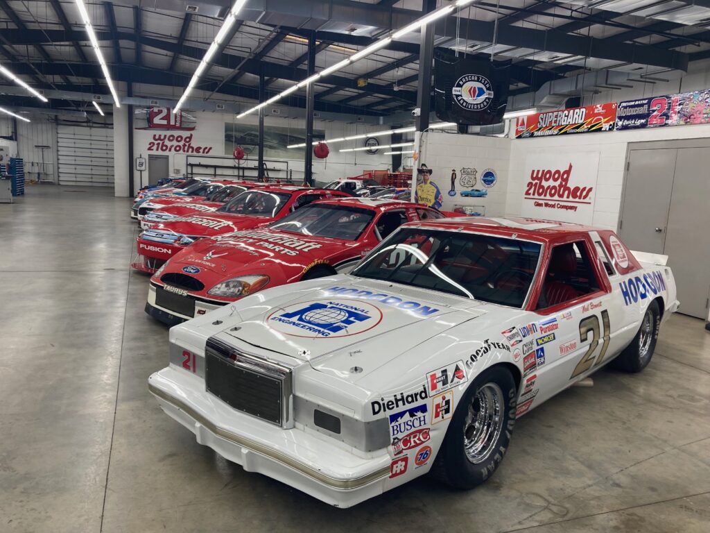 A line of old race cars are seen. The one closest to the camera is white, and the ones farther out are red.