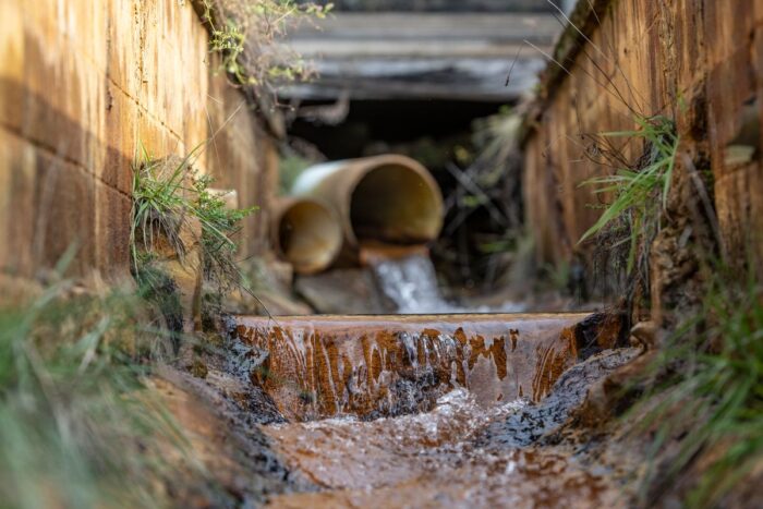 Water pours from a pipe into a small creek, giving it a rust-colored tint.