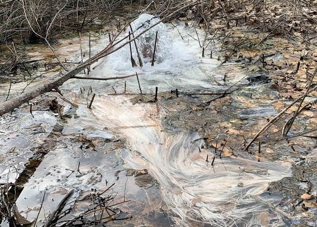 A photograph of a contaminated creek. The water is murky and gray.