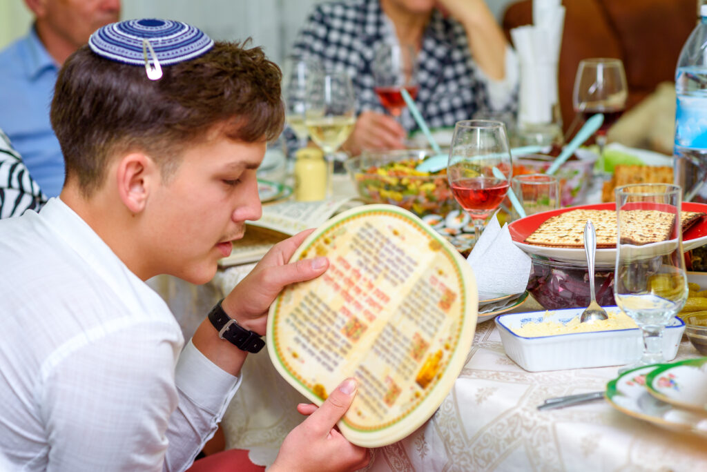 Young man in a white shirt reads from a book at a meal.