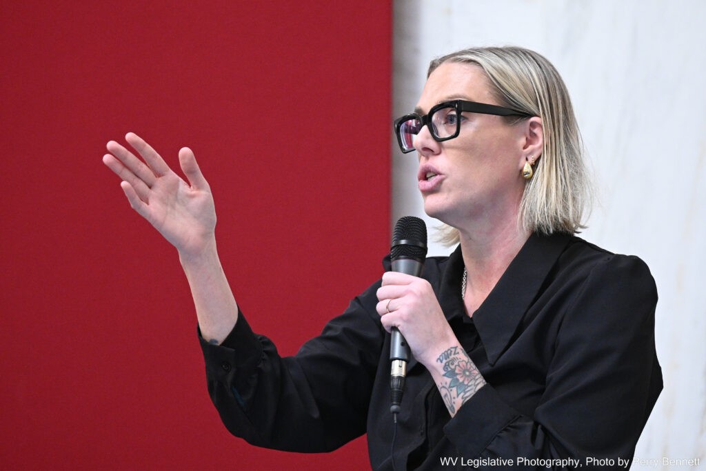 Blonde haired woman with black glasses speaking into a microphone