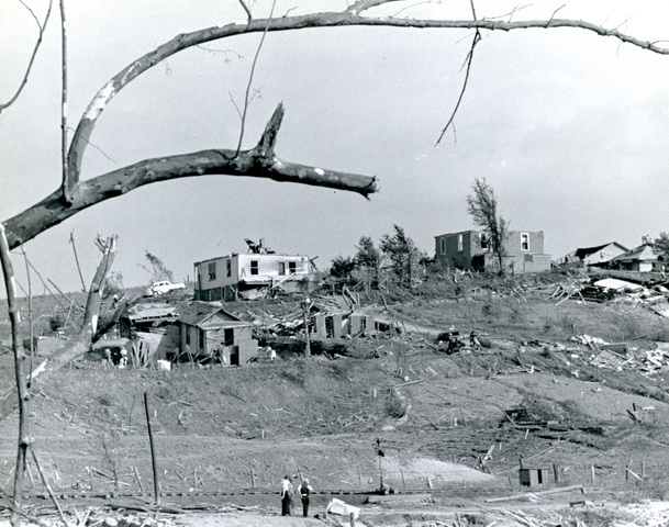 A black and white photo shows homes and trees damaged by a tornado.