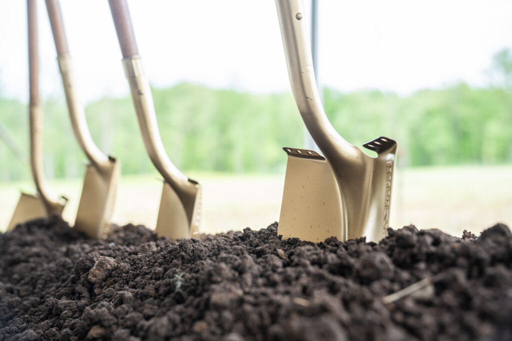 Golden shovels are seen lodged into a pile of dirt from a low angle.