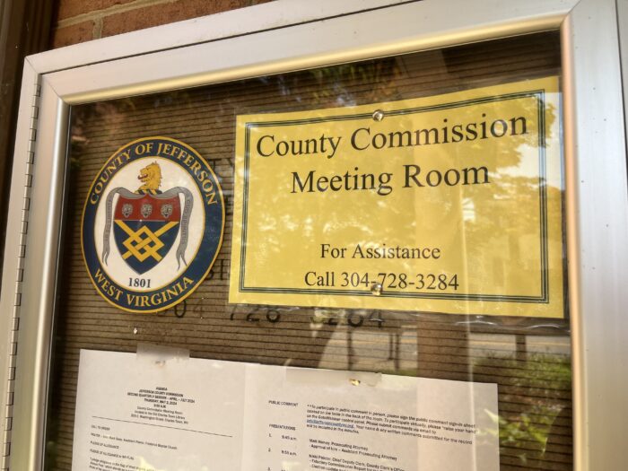 A sign reads "Jefferson County Commission Meeting Room." Beside it stands the county seal of Jefferson County. An agenda for a May 2 meeting is posted below it.