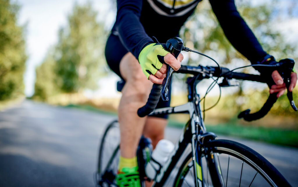 A close up photograph of an athlete on a bicycle. The person is wearing a black and green cyclist suit. Their face is out of frame.